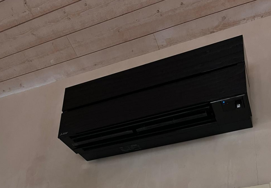 Unité intérieure de climatisation noire installée sur un mur sous un plafond en bois.