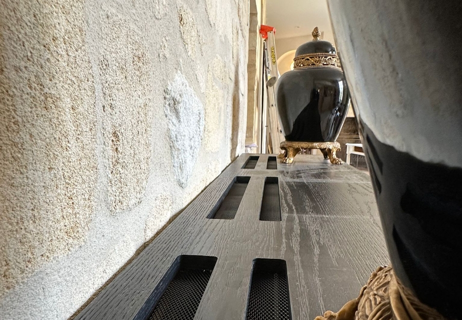 Grilles de soufflage noires intégrées dans un meuble le long d’un mur en pierre.