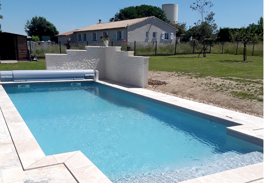 Piscine rectangulaire avec margelles claires et volet roulant dans un jardin.