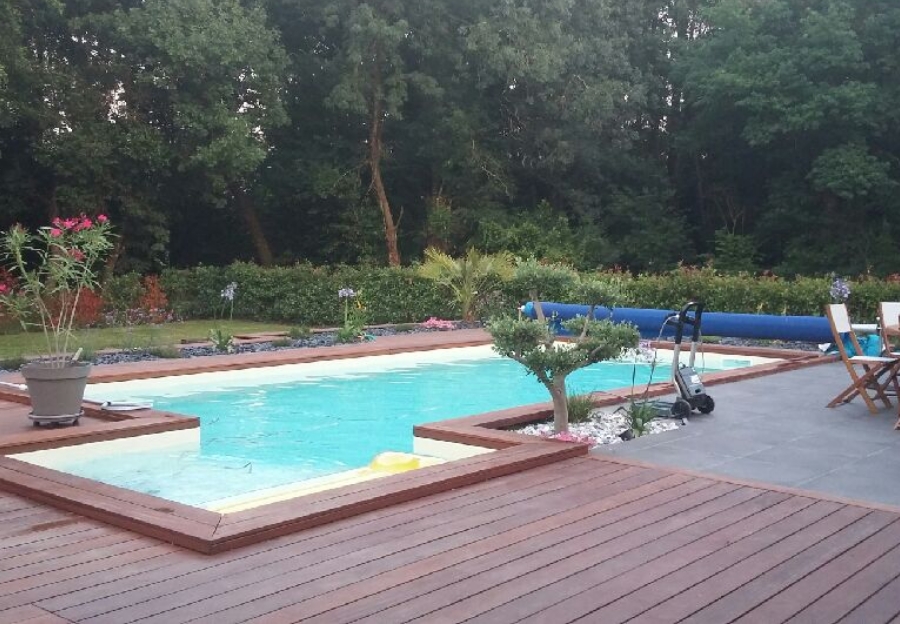 Piscine paysagée avec terrasse en bois au bord d’un espace boisé.