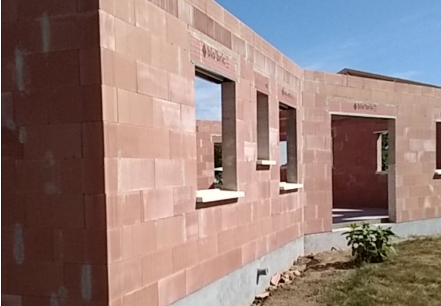 Construction d’une maison neuve en briques avec charpente en bois et véhicules PBC Groupe.